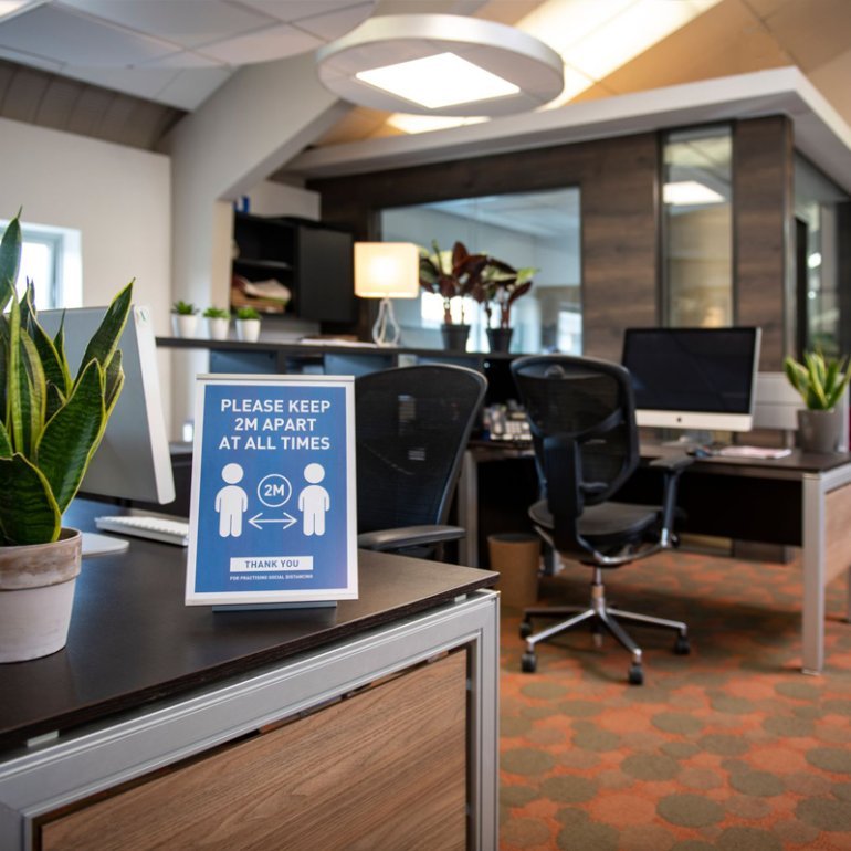 Bureau dans un environnement de bureau avec un détenteur absolu de l'étiquette autoportante pour afficher les règles de distanciation sociales.