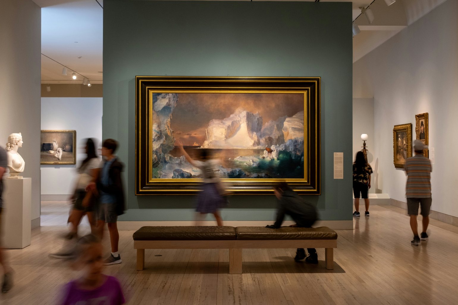 Large artwork and other pieces on display in a gallery with lots of people moving through the space